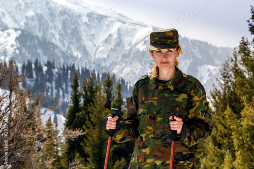 young woman in khaki uniform with walking sticks on a background of snow-capped mountains