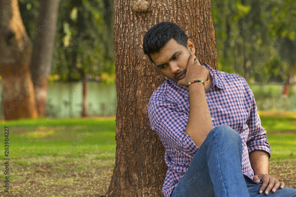 Young guy sitting and thinking leaning against tree Young guy sitting and thinking leaning against tree