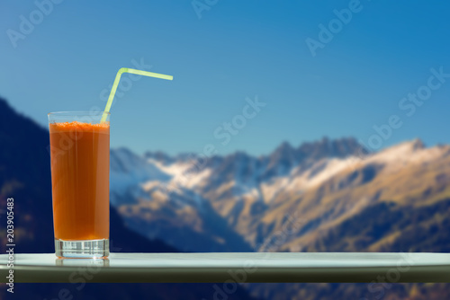 A glass of carrot juice with a straw in the cafe on the background of the Swiss Alps photo