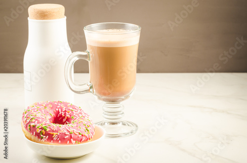 Coffee break: cappuccino, fresh sugary pink donut and white bottle/Coffee break: cappuccino, fresh sugary pink donut and white bottle. Selective focus and copyspace