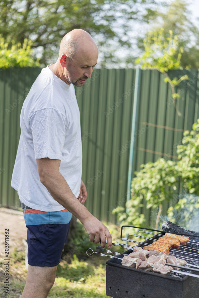 leisure, food, people and holidays concept - happy young man cooking meat on barbecue grill at outdoor summer party leisure, food, people and holidays concept - happy young man cooking meat on barbecue grill at outdoor summer party