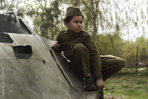 Boy in the military uniform on the tank of time of Second World War. Kids in uniform. Soldier boy. War time. photo