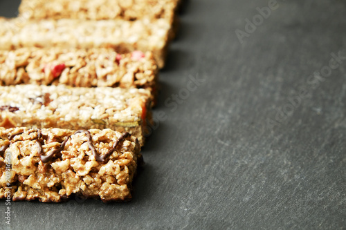 Row of mixed gluten free granola cereal energy bar with dried fruit & various nuts, gray concrete background. Healthy vegan super food, fitness dieting snack for sporty lifestyle. Top view, copy space