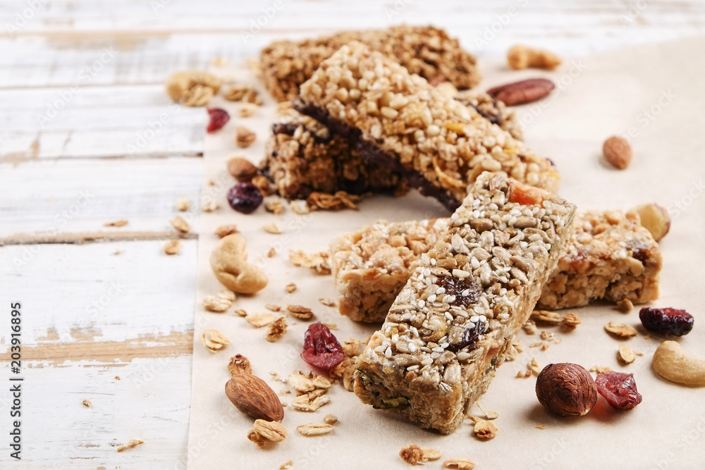 Various granola chocolate energy bars in row with scattered mixed nuts, cereals & dried fruit, grunged white wood table background. Healthy vegan fitness food snack. Top view, copy space, close up. Various granola chocolate energy bars in row with scattered mixed nuts, cereals & dried fruit, grunged white wood table background. Healthy vegan fitness food snack. Top view, copy space, close up.