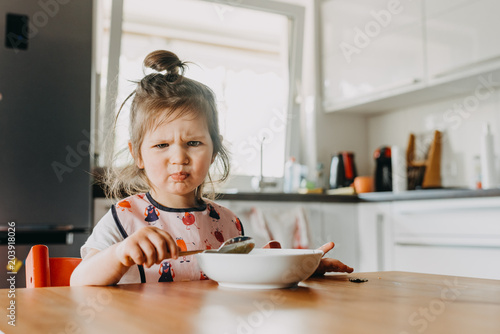 adorable funny toddler girl looks unhappy with her meal