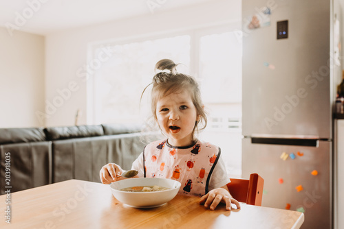 adorable funny toddler girl eating soup at the modern open kitchen