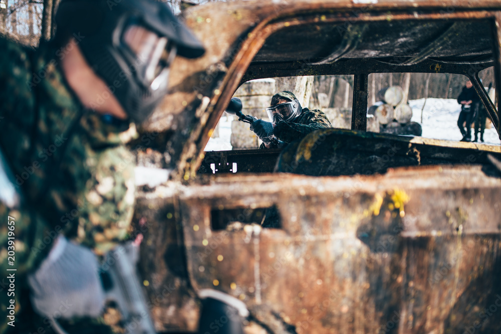 Paintball battle, players fight around burned car