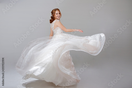 Young woman spinning in a curvy wedding dress. woman bride in lavish wedding dress. Light background.