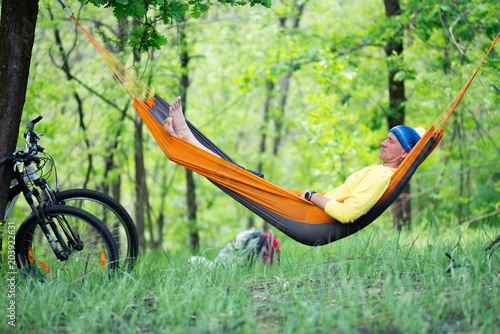 Tired man relaxes and meditates in a hammock after biking