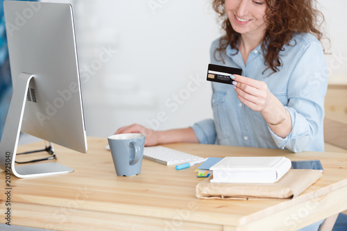 Cropped shot of incomprehensible girl in blue shirt holding debit card making payment while shopping online photo