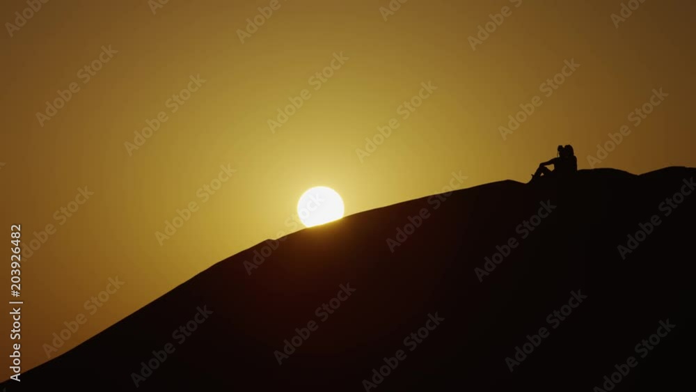 People sitting at sunset on top of a dune People sitting at sunset on top of a dune