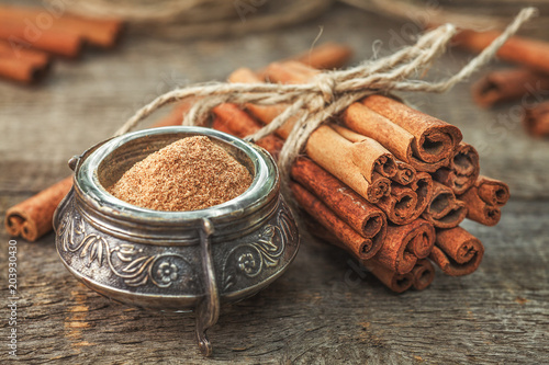 Ground cinnamon, cinnamon sticks, tied with jute rope on old wooden background in rustic style