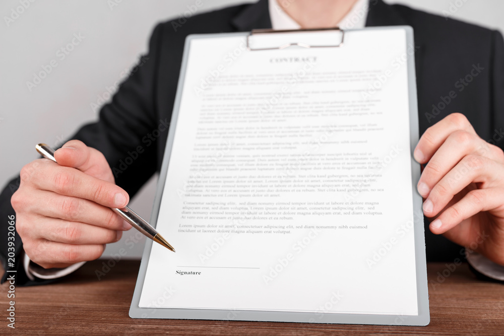 Businessman indicates the place for signing in the contract,which is attached to a clipboard. Businessman indicates the place for signing in the contract,which is attached to a clipboard.
