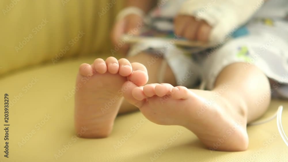 Thai child playing smartphone on chair, focus on child’s feet Thai child playing smartphone on chair, focus on child’s feet