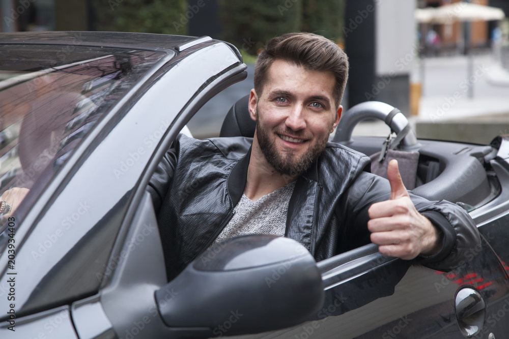 Young happy businessman in a cabriolet is pointing his thumb up. Young happy businessman in a cabriolet is pointing his thumb up.