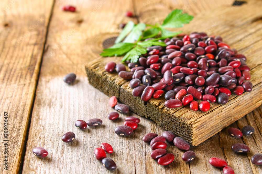 Red raw beans with greens on a wooden table.