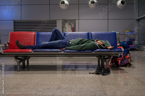 young tourist man with a backpack is sleeping in a airport waiting for an airplane because of flight delays