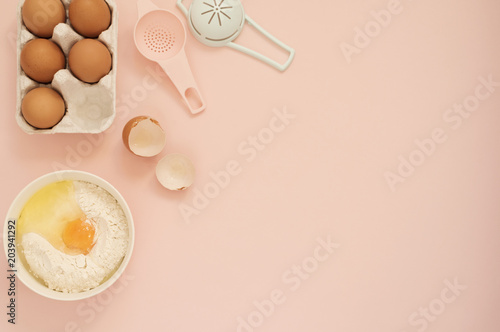 Ingredients and kitchen bake tools for cooking cake or sweets - eggs, flour on a pastel punchy pink background. Top view of a holiday baking still life