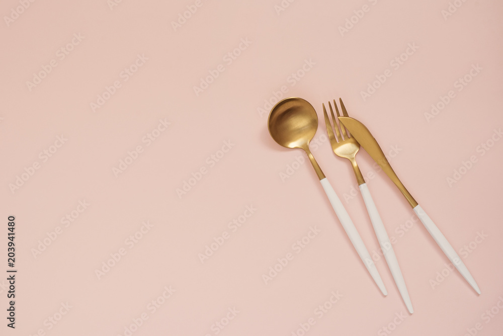 Gold cutlery. Golden spoon set, golden knife, spoon and fork on the table. Luxury spoon set top of view. Pastel punchy pink background