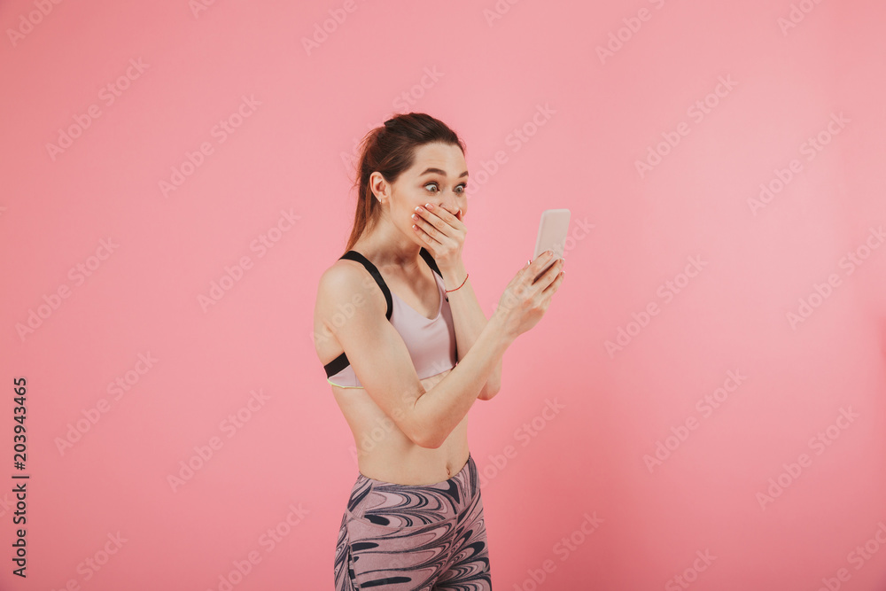Surprised joyful sportswoman using smartphone while covering her mouth Surprised joyful sportswoman using smartphone while covering her mouth