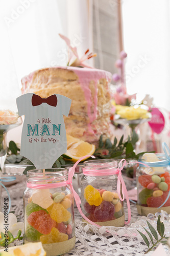 Baby shower party dessert table with is a cake, candies, marshmallows, cakepops, fruits, juice and flowers. Details, close-up. The inscription "This is a boy" on a greeting card