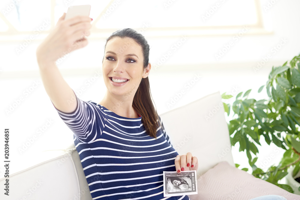 Happy pregnant woman making selfie with her 3d ultrasound picture of her baby Happy pregnant woman making selfie with her 3d ultrasound picture of her baby