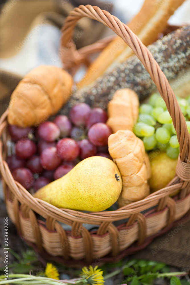 freshness, health, food concept. there is marvelous handmaded basket prepared for picnic in the garden, it is full of fruits such as green and red grape and pears, and few croissants