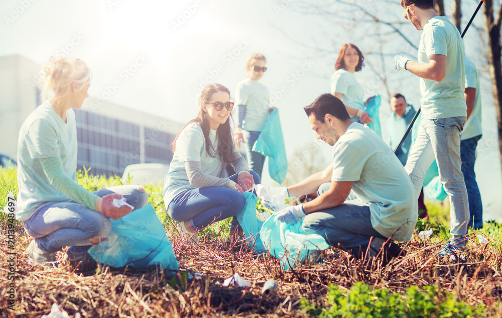 Fototapeta premium volunteering, charity, cleaning, people and ecology concept - group of happy volunteers with garbage bags cleaning area in park