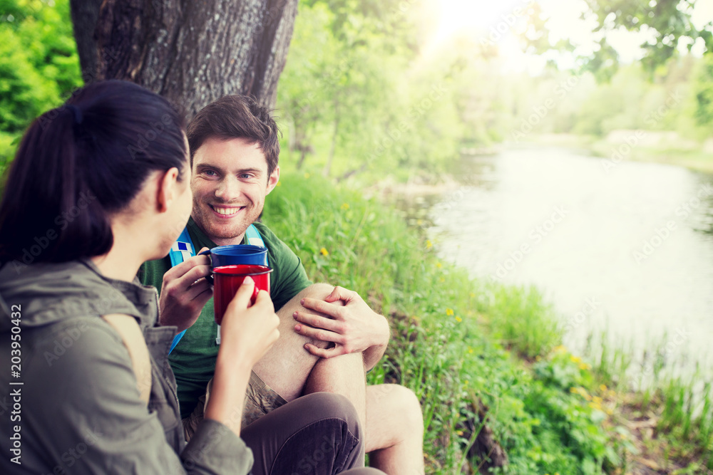 travel, tourism, hike, camping and people concept - happy couple with cups drinking tea in nature on river bank travel, tourism, hike, camping and people concept - happy couple with cups drinking tea in nature on river bank