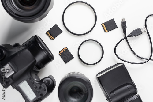 top view of modern dslr photo camera, lenses and equipment over white table