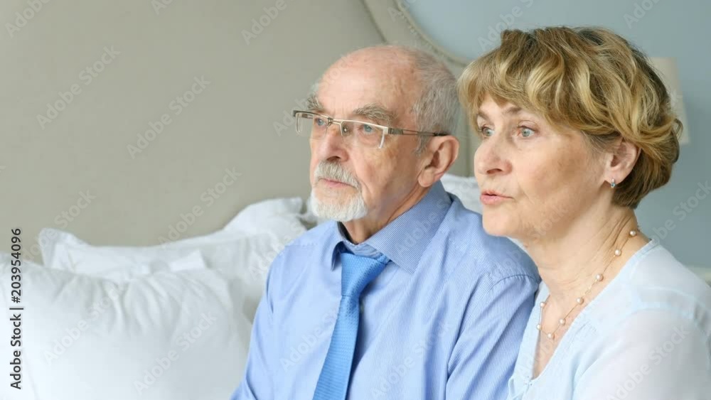 Portrait elderly couple sitting in bedroom and looking out the window, conversation of old couple Portrait elderly couple sitting in bedroom and looking out the window, conversation of old couple