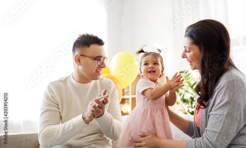 family, holidays and people concept - mother, father and happy little daughter clapping hands at home birthday party