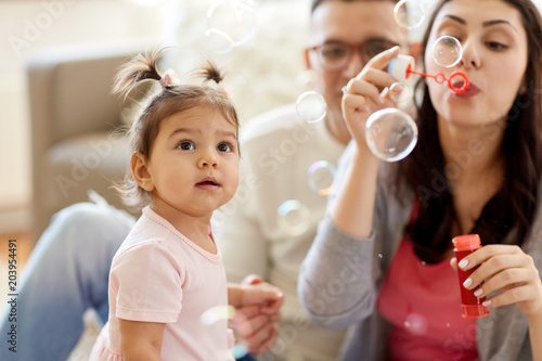 family  childhood and people concept - happy mother blowing soap bubbles and playing with little daughter at home
