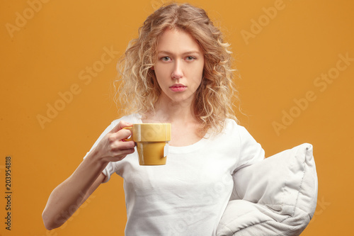 Sleepy girl with a cup of tea and a pillow on a yellow background.