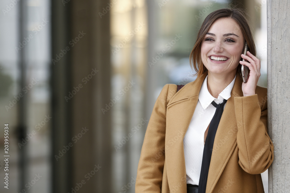 Manager vestita con cappotto beige camicia bianca e cravatta nera , parla divertita al telefono fuori dal suo uffico Manager vestita con cappotto beige camicia bianca e cravatta nera , parla divertita al telefono fuori dal suo uffico