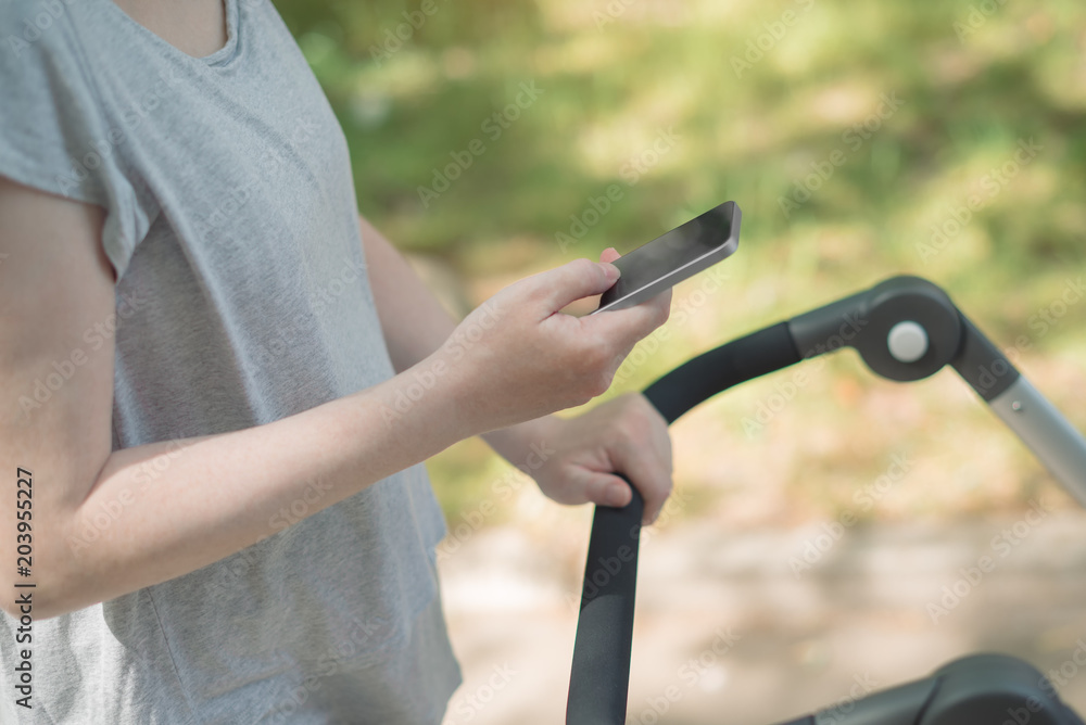 Mother pushing baby stroller and reading text message on smartphone