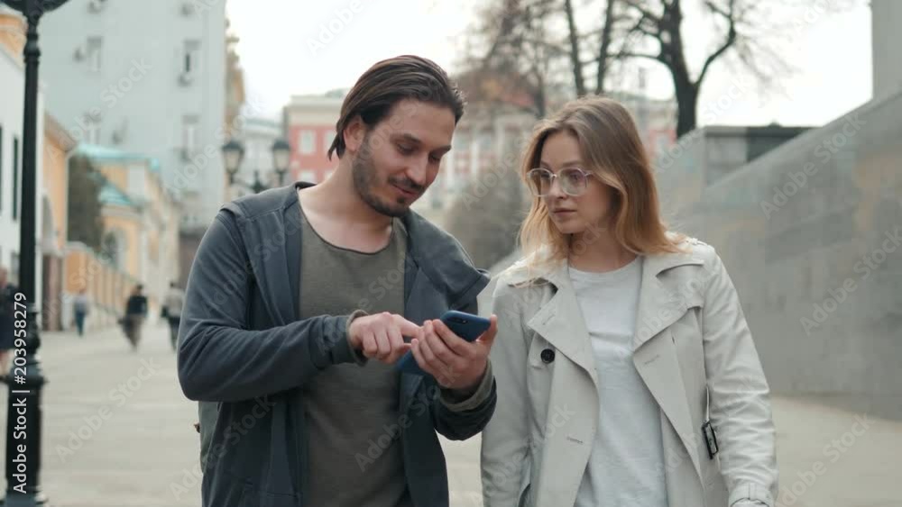 Couple of tourists walking in a city street with phone use navigation applications, man and woman tourist walk Couple of tourists walking in a city street with phone use navigation applications, man and woman tourist walk