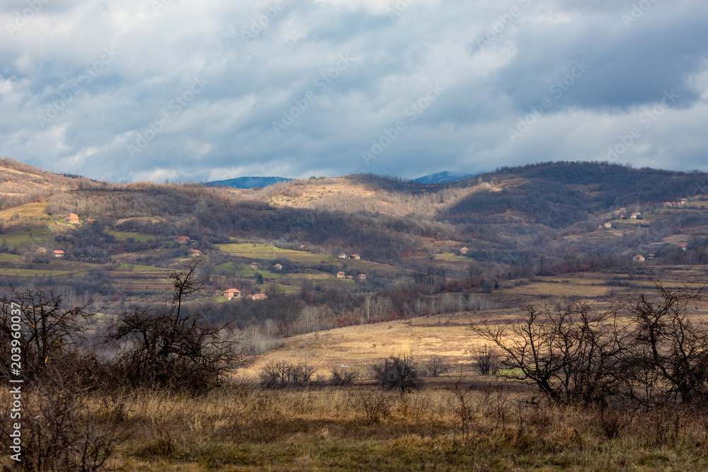 Tranquil Serbian countryside landscape with several country houses, hills and leafless bushes. Cloudy autumn sky
