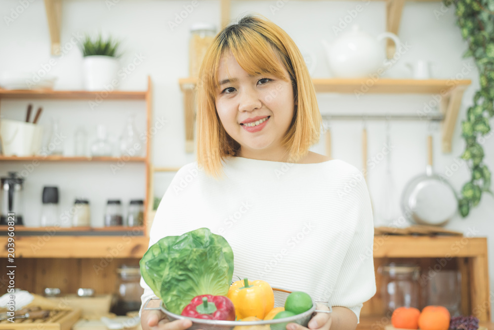 Smiling asian beautiful woman sitting in the kitchen at home and holding a salad bowl. Young happy female eating healthy salad with green fresh ingredients for healthy body.