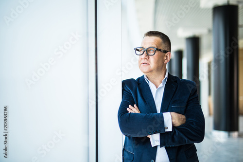 Seniow businessman with crossed hands standing and thinking by the panoramic windows in office.