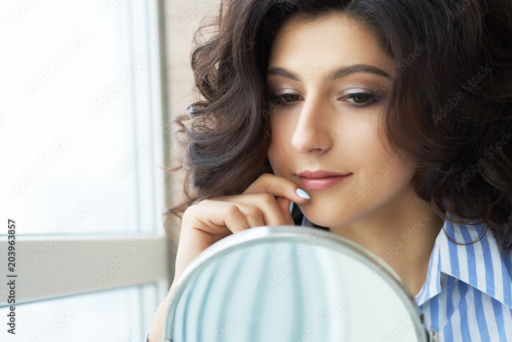 Reflection of the hairstyle of the female client in mirror. Concept of fashion and beauty. Beautiful brunette with lush hair looks at the result of the work of the stylist. Reflection of the hairstyle of the female client in mirror. Concept of fashion and beauty. Beautiful brunette with lush hair looks at the result of the work of the stylist.