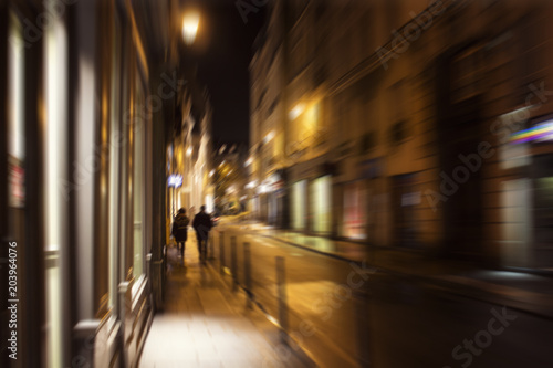 Blurry motion image of people walking on street at night in Paris.