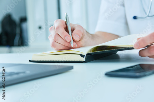 Male doctor or medical student holding ballpoint pen and writing on notepad. Therapist fills the patient admission schedule