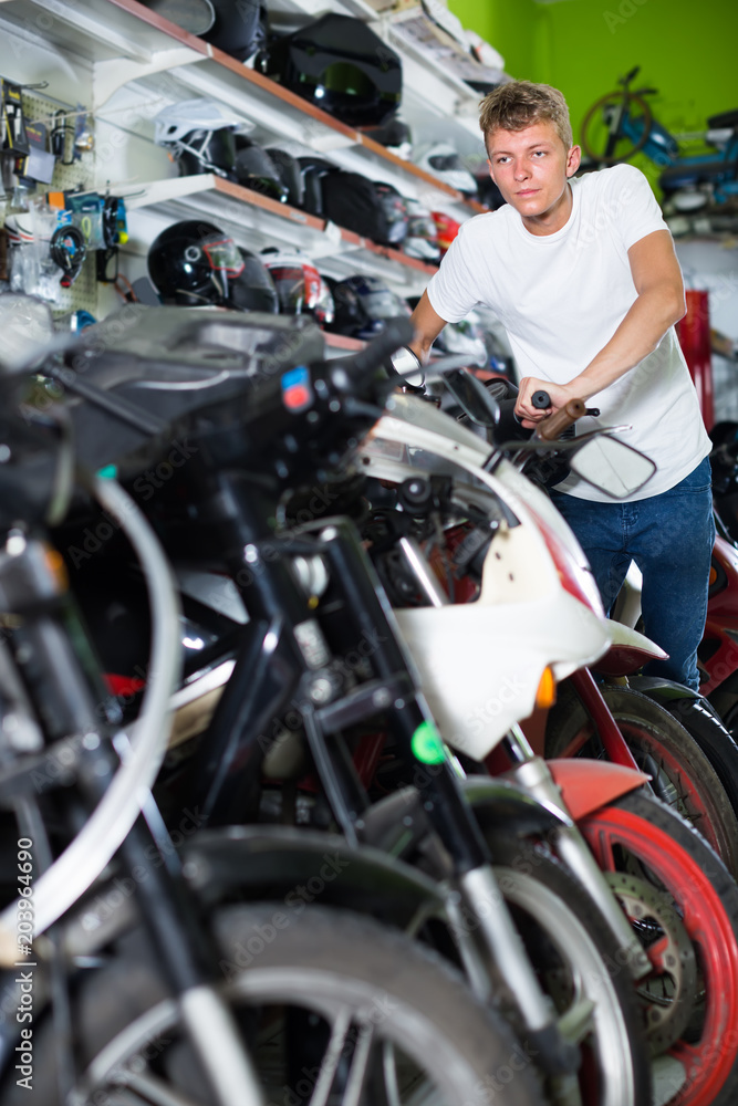 Young positive man motorcyclist choosing the bike in the shop