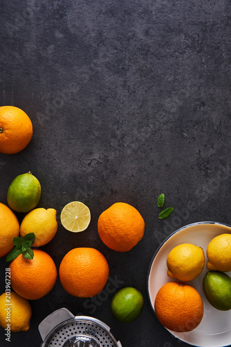 Top view of fresh ripe citruses. Lemons, limes, oranges and grapefruits with glasses and citrus squeezer on dark concrete background. Flat lay with copy space.