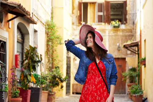 Smiling pretty tourist woman holding hat and looking away at Trastevere in Rome, Italy.