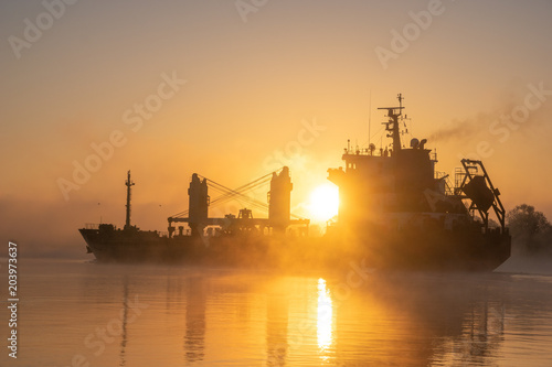 merchant ship sailing down the river in the mist at sunrise