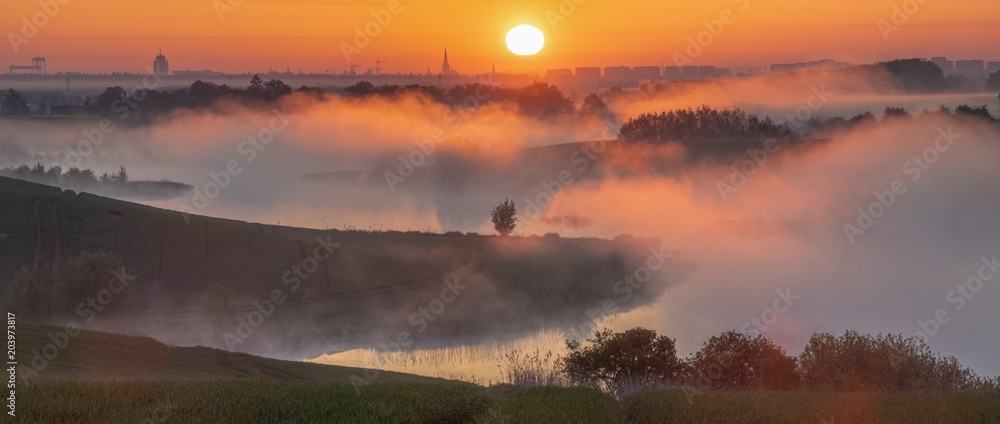 misty sunrise over a lake surrounded by green hills
