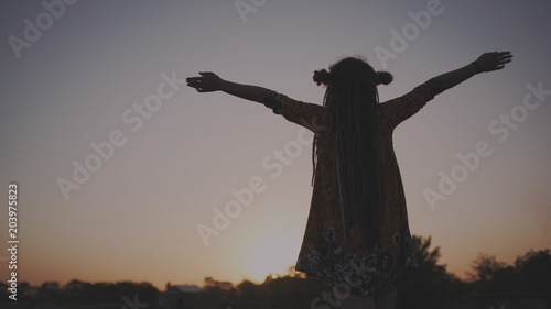 Silhouette of hippie woman with dreadlocks raising arms to sky