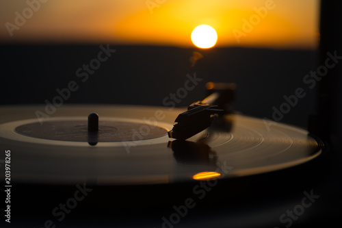 Turntable vinyl record player on the background of a sunset over the mountains. Sound technology for DJ to mix & play music. Black vinyl record. Vintage vinyl record player.